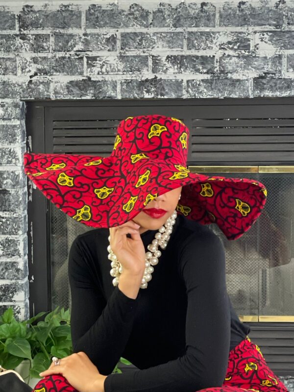 A woman wearing a hat and pearls in front of a fireplace.