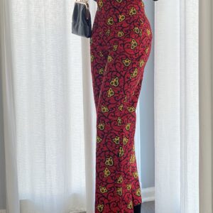 A woman standing in front of a window wearing red and yellow floral print pants.