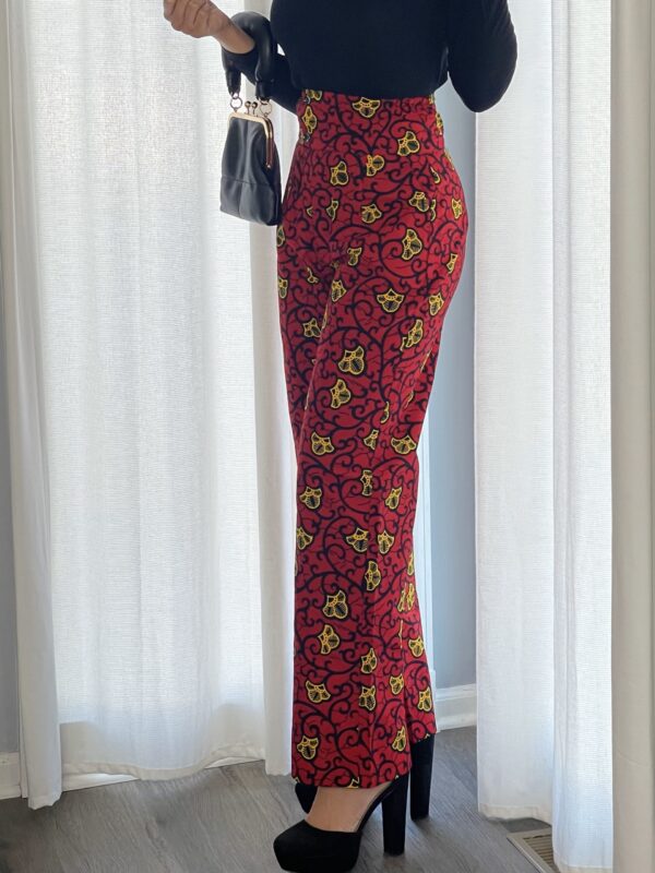 A woman standing in front of a window wearing red and yellow floral print pants.