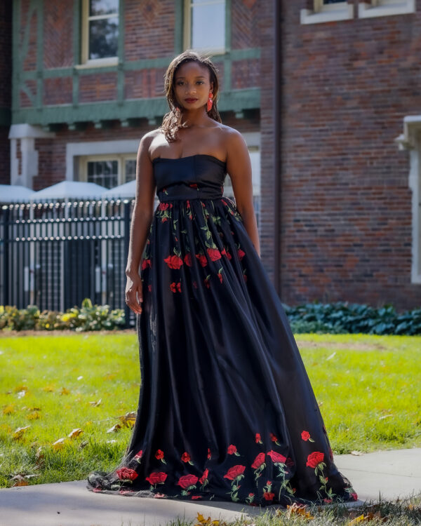 Woman in black floral gown stands outside.