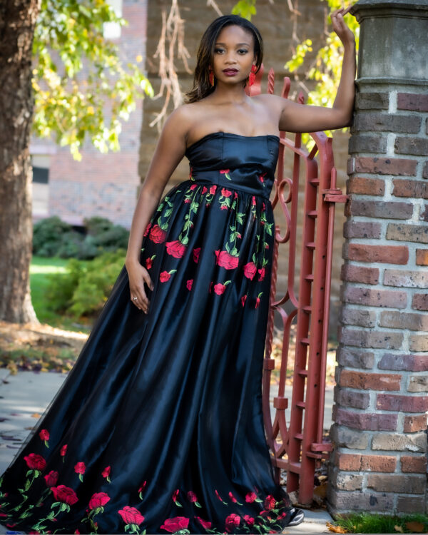 Woman in a black floral gown by a gate.