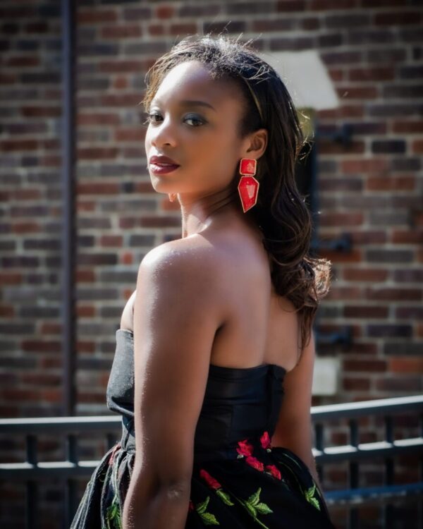 A woman in black dress standing next to brick wall.