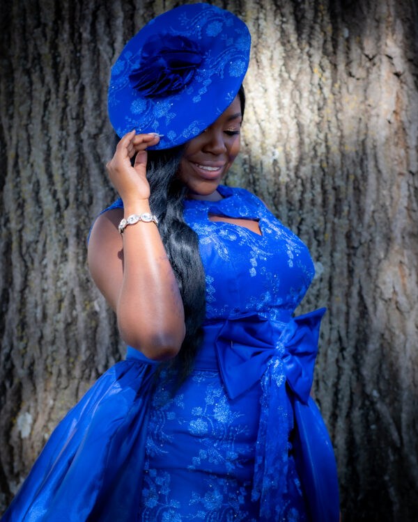 Woman in blue dress and hat smiling.