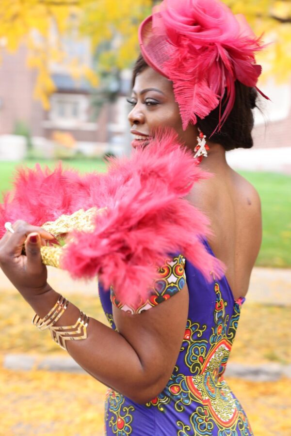 Woman in purple dress holding a feathered fan.