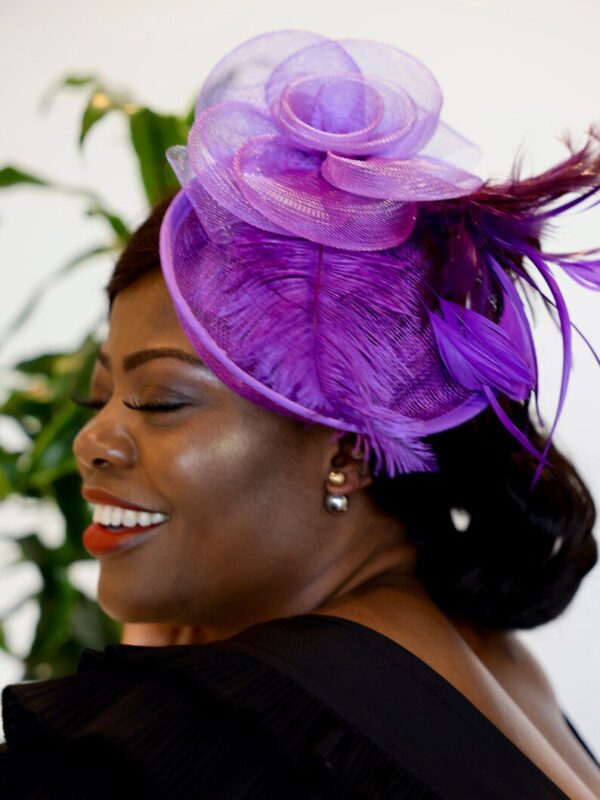 Woman in a purple feathered hat smiling.