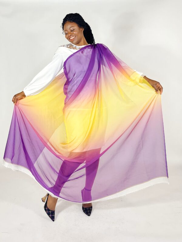 Woman in white dress holding a purple and yellow shawl.