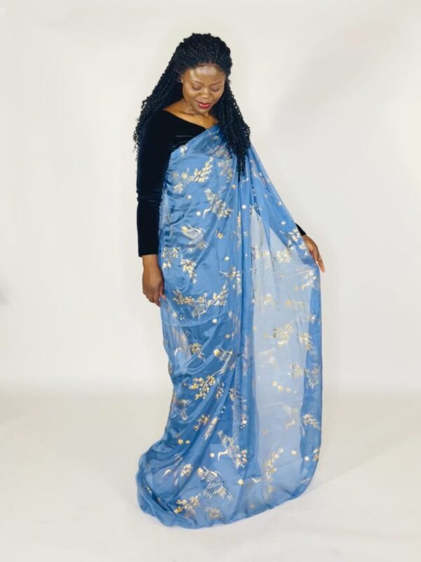 A woman standing in front of a white wall wearing a blue floral print sari.