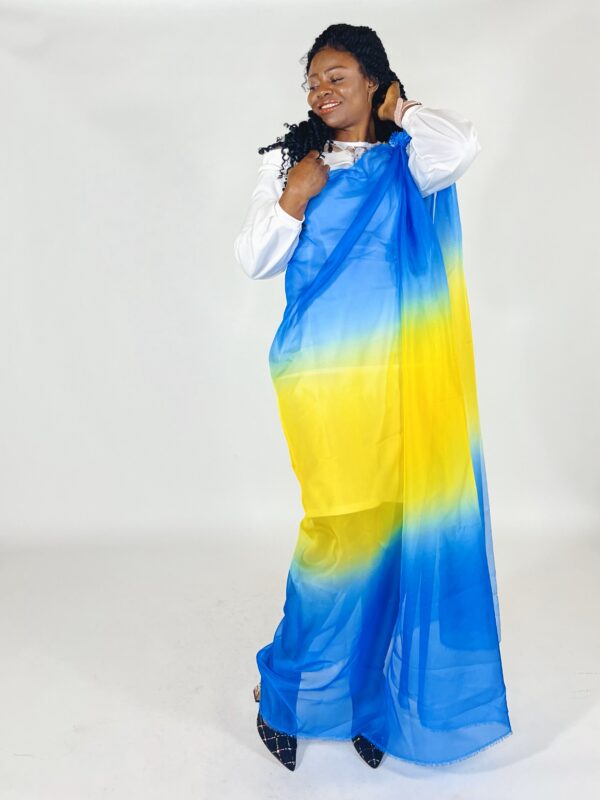 A woman in blue and yellow dress standing next to wall.